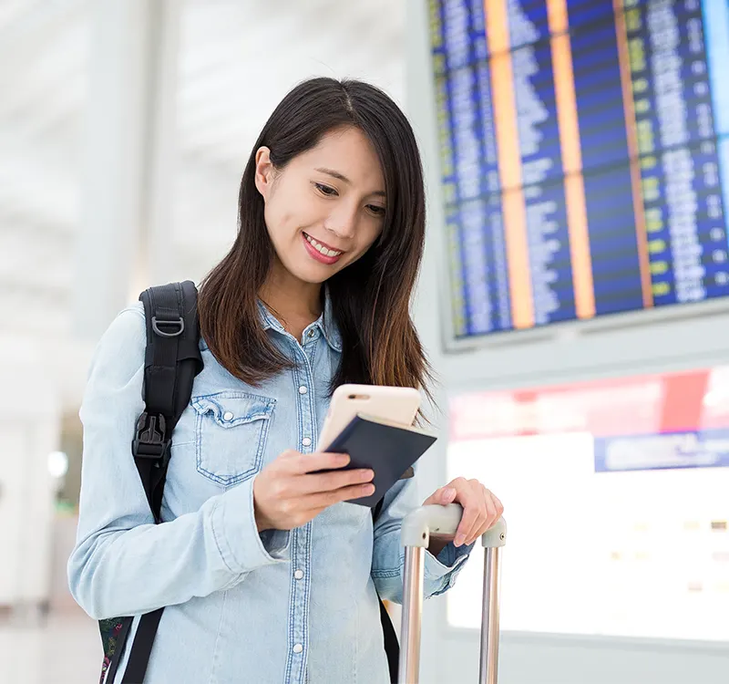 A traveller checking her phone beside a flight information board
